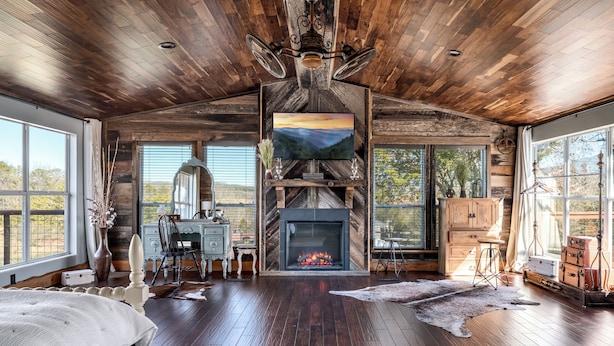Interior rústico de una cabaña con chimenea, pisos de madera y grandes ventanales con vistas panorámicas.