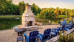 Una chimenea de piedra con asientos, un estanque y una terraza de madera con sillas tipo Adirondack.