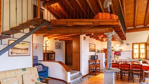 A spacious living area with a wooden staircase, a stone pillar, and a dining area with a red tablecloth.