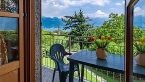 A balcony with a table and chairs, a potted plant, and a view of mountains and trees.