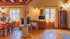 A cozy room with a stone pillar, wooden beams, a dining area with a table and chairs, a TV, and a cabinet.