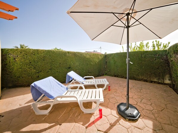 Un patio con dos sillones de descanso, un gran paraguas y una botella de agua en el suelo.