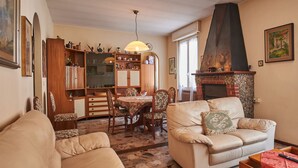A cozy living room with a fireplace, a dining area with wooden furniture, and a large window.