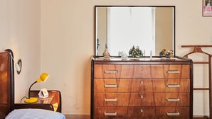 A bedroom with a wooden dresser, a bed with a striped pillow, a nightstand with a lamp, and a mirror on the wall.