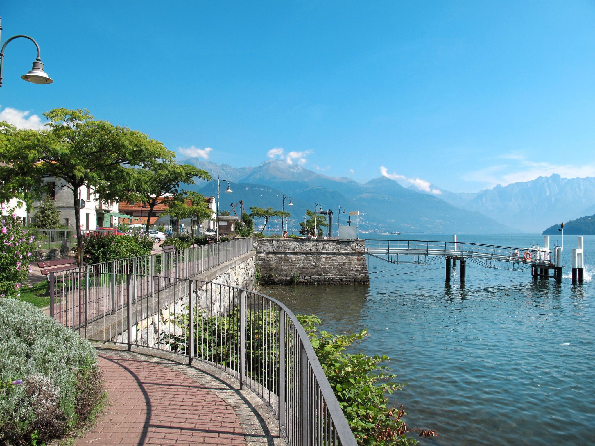Eine Uferpromenade mit einer Steinmauer, Metallgeländer und einer Brücke zu einem Steg.