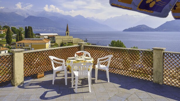 A terrace with a table and chairs overlooking a lake, with mountains in the background.