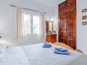 A bedroom with a bed, a wooden wardrobe, a vanity with a mirror, and a window with curtains.