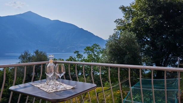 A table with three wine glasses and a bottle on a balcony with a mountain view. - Ruscello by Interhome (San Siro)