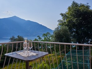 Een tafel met drie wijnglazen en een fles op een balkon met uitzicht op een berg.