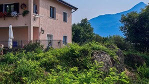 A two-story house with a balcony, a mountain in the background, and lush greenery in the foreground. - Ruscello by Interhome (San Siro)