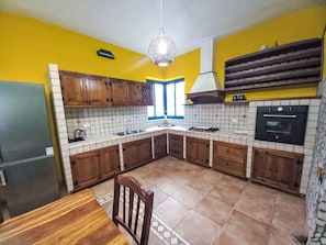 Eine Küche mit Holzausstattung, einer gefliesten Spritzschutzwand, einem eingebauten Backofen und einem Esstisch mit Stühlen.
