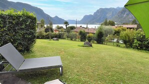 A grassy outdoor area with a table and chairs, surrounded by trees and a view of mountains and a lake. - Villa Vesta by Interhome (Lago d'Idro)