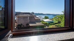 Udsigt fra et vindue over et hus med swimmingpool, omgivet af grøn vegetation og bakker.