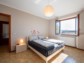 A bedroom with a bed, bedside tables, a lamp, a radiator, and a window with a view. - Monte San Giulio by Interhome (Orta San Giulio)