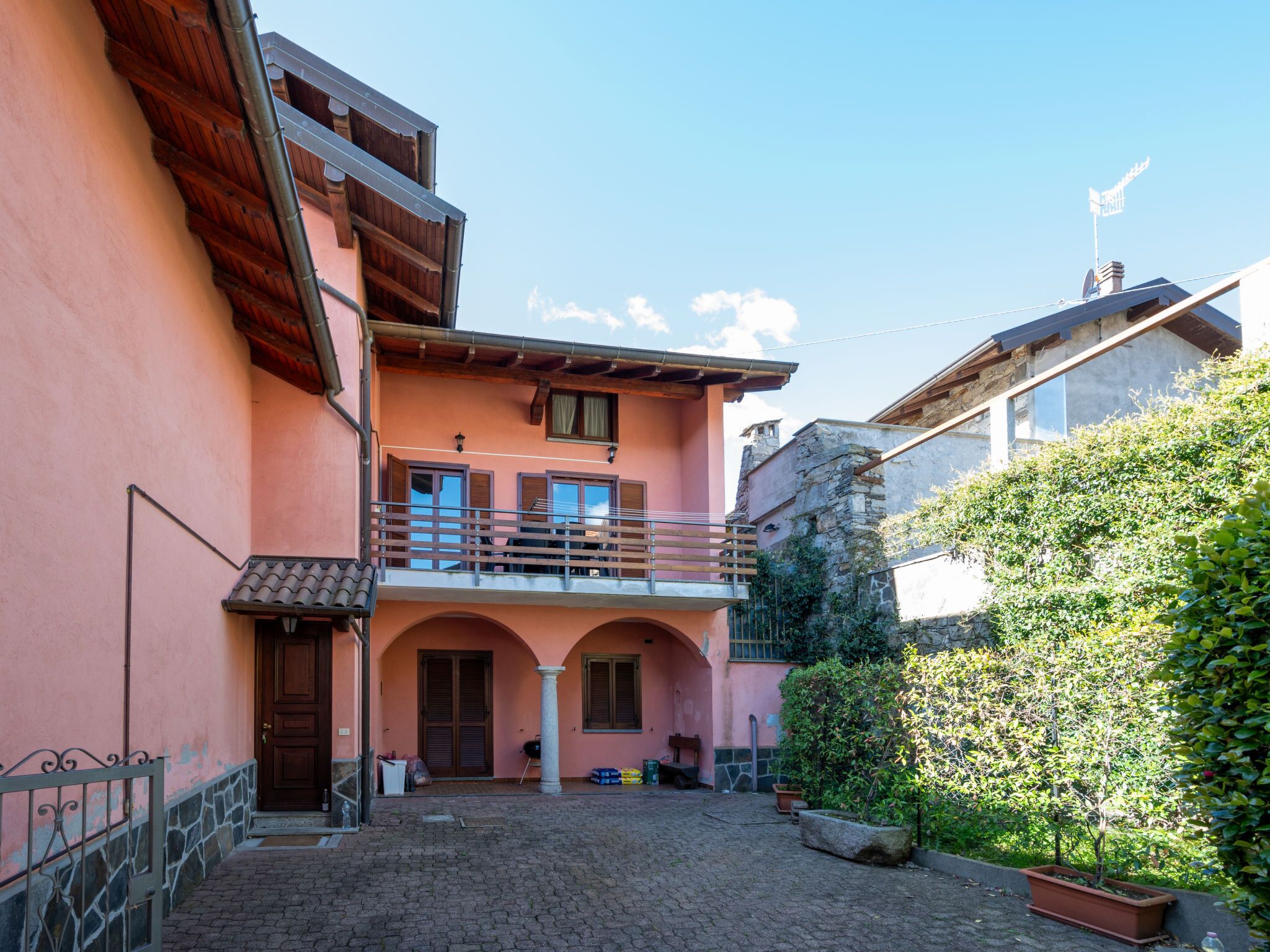 A courtyard with a pink building, a stone wall, and a wooden balcony.