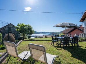 A patio with outdoor seating, a table with a large umbrella, and a view of a lake and mountains. - Monte San Giulio by Interhome (Orta San Giulio)