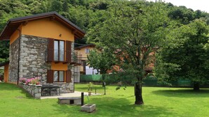 Un bâtiment à deux étages, doté d’une façade en pierre et de volets en bois, entouré d’une pelouse bien entretenue et d’arbres.
