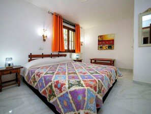 Ein Schlafzimmer mit einem großen Bett, einem Nachttisch, einer Fenster mit Vorhängen, einer Wandlampe und einem Gemälde.