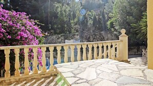 Eine terrasse mit steinbelagten Fliesen und einer Balustrade, umgeben von üppigem Grün und blühenden Pflanzen.