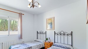 A bedroom with two beds, a radiator, a wooden nightstand, a framed picture, and a window with curtains. - Altamar by Interhome (Calpe/Calp)
