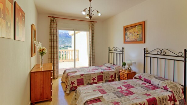 A bedroom with two beds, a wooden dresser, a nightstand, a lamp, and a painting on the wall. - Altamar by Interhome (Calpe/Calp)