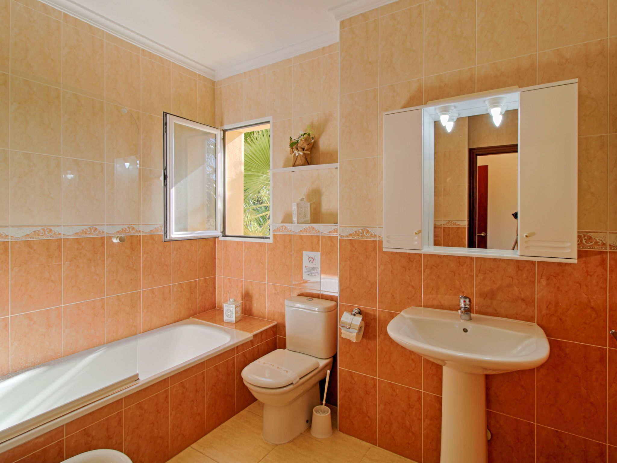 Un baño con bañera, inodoro, lavabo y ventana con vista a zonas verdes.