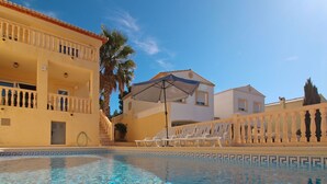 A clear swimming pool with lounge chairs and umbrellas, surrounded by buildings with balconies and palm trees. - Altamar by Interhome (Calpe/Calp)