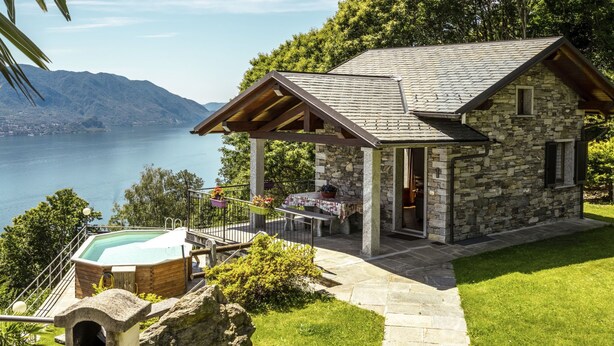 Une maison en pierre avec une piscine, entourée d’une végétation luxuriante et offrant une vue sur un lac.