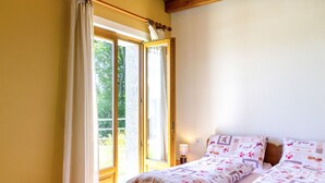 Une chambre avec deux lits, une fenêtre avec des rideaux, une lampe de chevet et une vue sur la verdure.