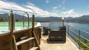 Un espace aménagé au bord de la piscine, avec vue sur les montagnes, une terrasse en bois et du mobilier d’extérieur.