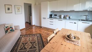 A modern kitchen with white cabinets, a wooden dining table, and a patterned rug. - Il Ciliegio by Interhome (Maccagno con Pino e Veddasca)
