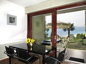 A dining area with a black table, four chairs, a vase with sunflowers, and a view of the sea through an open door. - Euroville by Interhome (Luino)