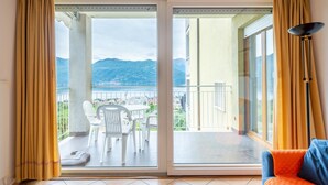 A balcony with a table and chairs, a sofa, and a view of mountains and a lake. - Euroville by Interhome (Luino)