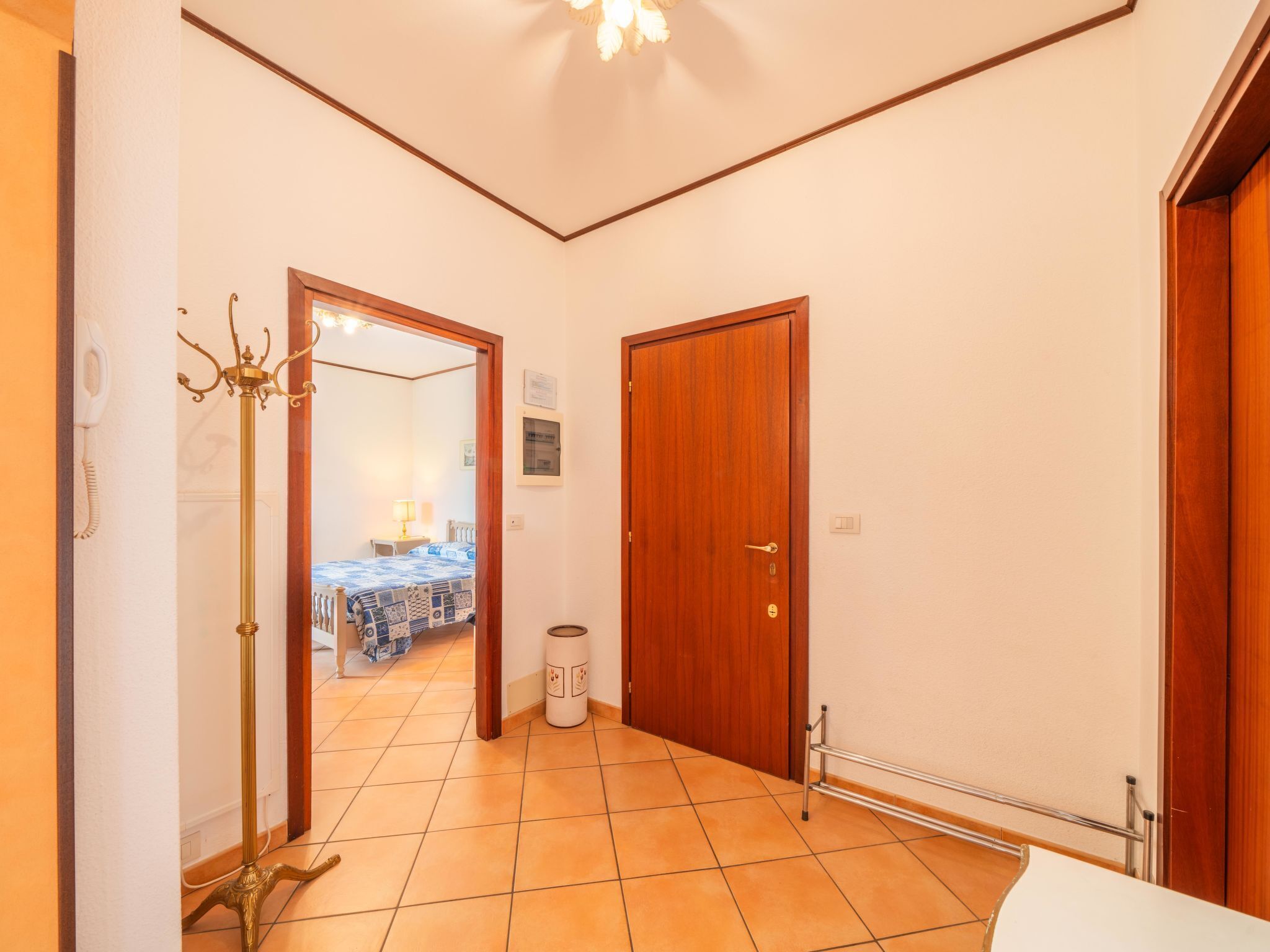 Un couloir avec un sol carrelé, une porte en bois, un radiateur et une poubelle.