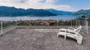 A terrace with a view of a lake and mountains, featuring white chairs and a railing. - Euroville by Interhome (Luino)