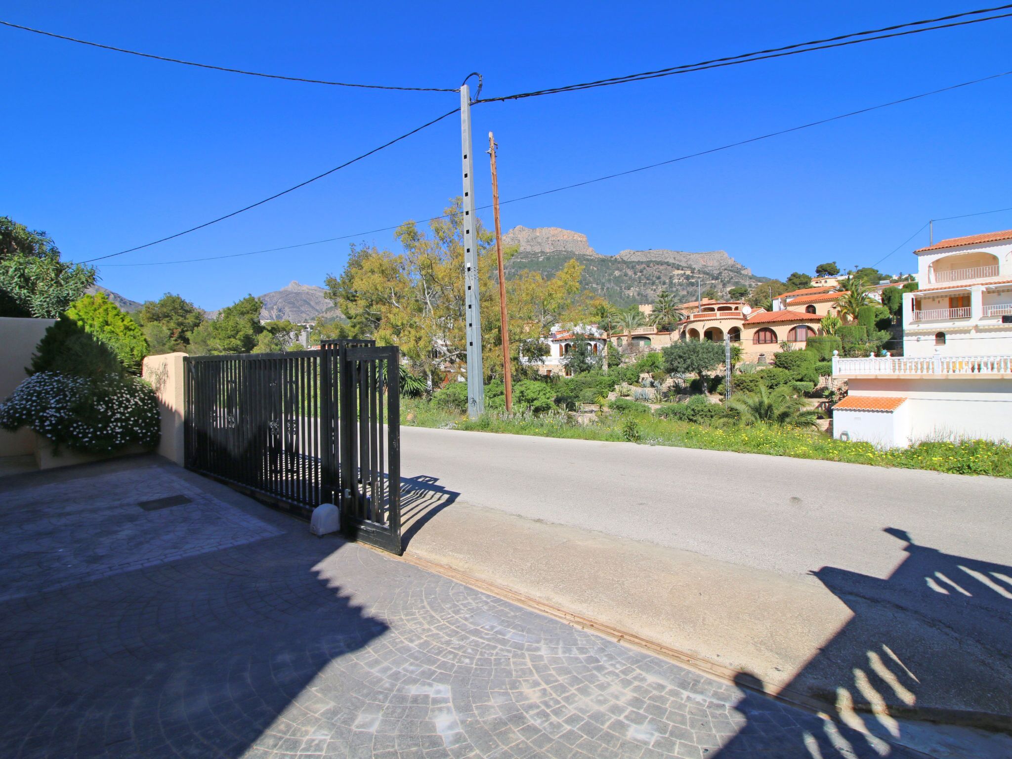Een woonstraat met een hekpoort, een verharde weg en huizen in mediterrane stijl.