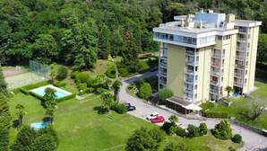Un edificio de varios pisos con balcones, rodeado de abundante vegetación y una cancha de tenis.