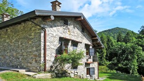 Ein Haus aus Stein mit geneigtem Dach und Schornstein, umgeben von viel Grün und Hügeln.