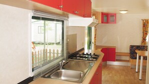 Une cuisine de taille réduite, équipée d’un évier, d’une cuisinière et de placards rouges.