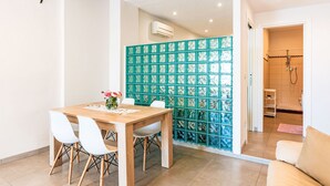 Ein modernes Interieur mit einem Holzesstisch, weißen Stühlen, einem türkisfarbenen Raumteiler und einem Duschbereich.