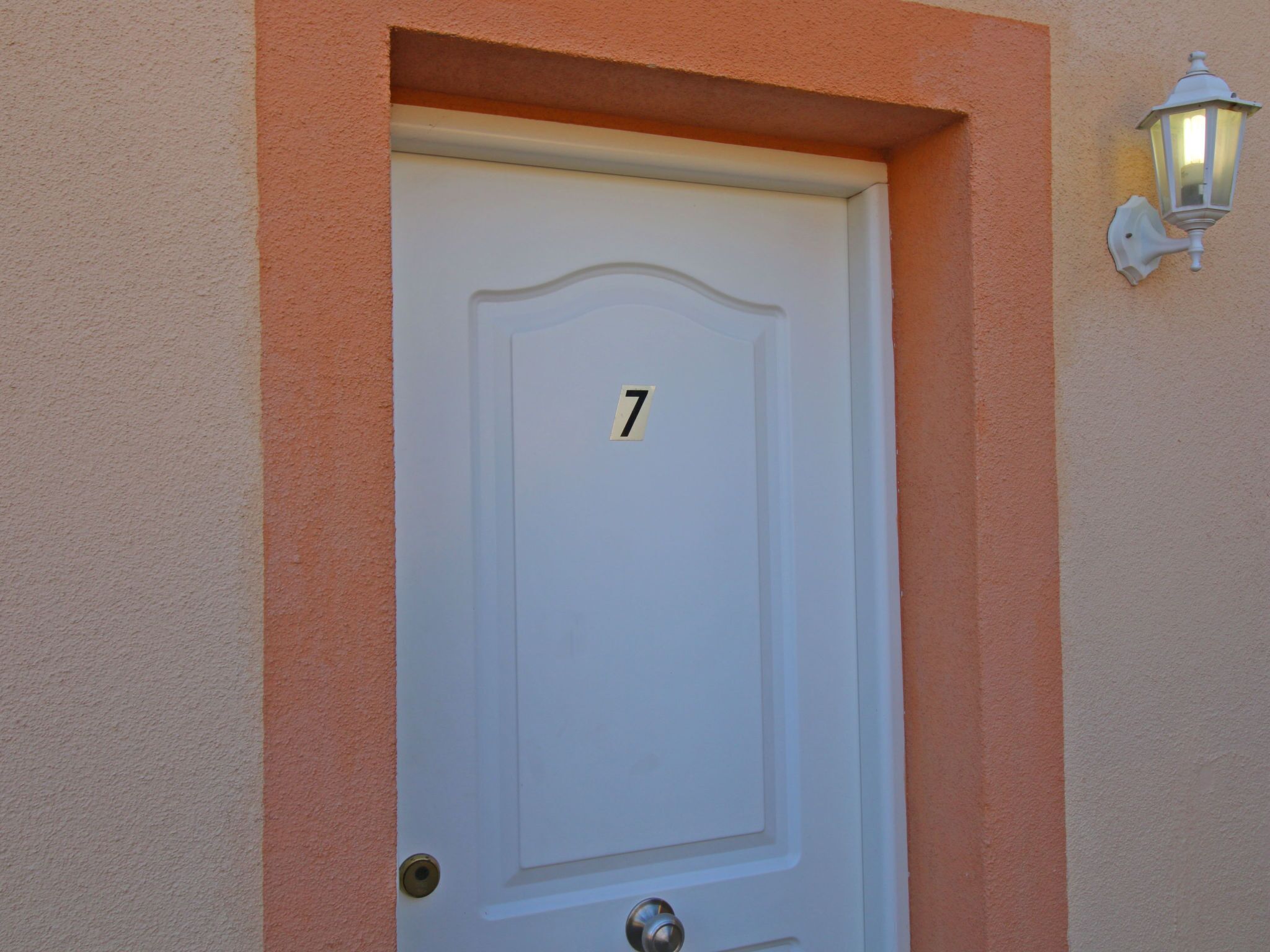 A white door with the number 7, a wall-mounted light fixture, and a textured wall.