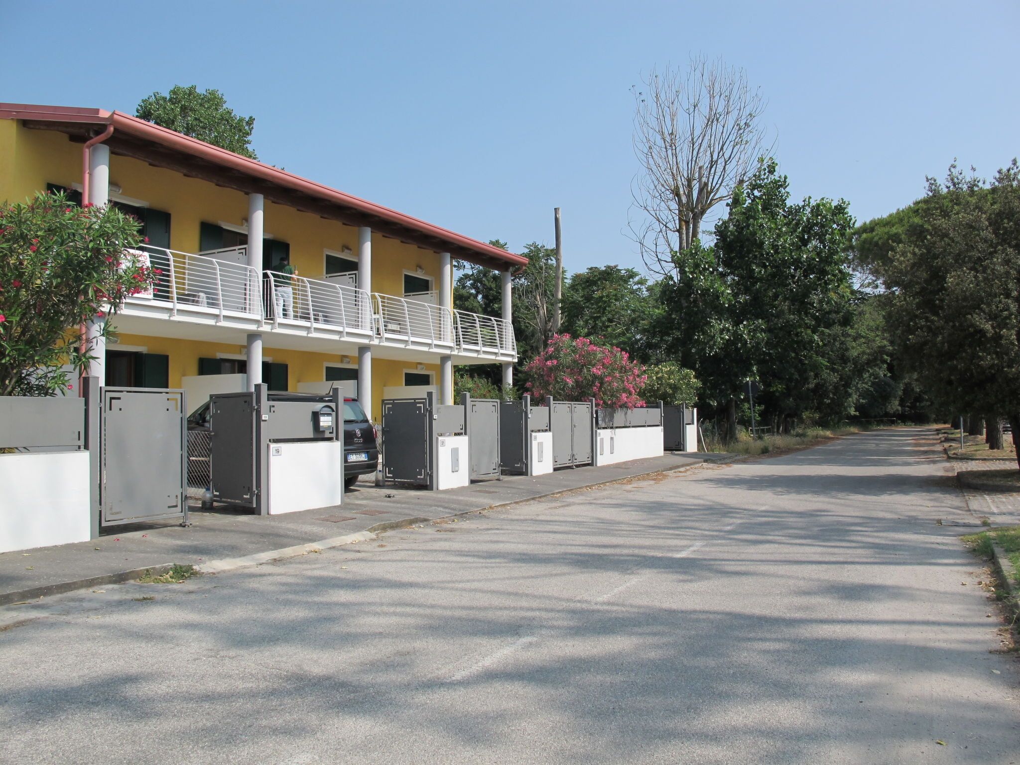 Ein gelbes Gebäude mit einem Balkon, großen Metalltoren und einem geparkten Fahrzeug.