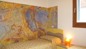 Un dormitori amb dos llits, un quadre abstracte gran a la paret i una finestra amb marc de fusta.