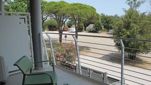 A balcony with two green chairs, a white wall, and a view of a parking lot with trees and flowers. - Vacation home Malva by Interhome (Lido di Volano)