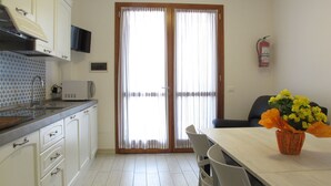 A modern kitchen with white cabinets, a microwave, and a sink. There is a dining area with a table and chairs, and a fire extinguisher mounted on the wall. - Vacation home Malva by Interhome (Lido di Volano)
