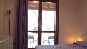 A bedroom with a bed, a window with curtains, a radiator, and a chair outside the window. - Vacation home Malva by Interhome (Lido di Volano)