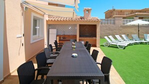 Area pranzo all'aperto con un tavolo lungo e sedie, un barbecue integrato e un angolo cottura.
