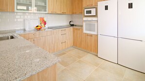 Una cucina moderna con mobili in legno, un piano di lavoro in granito, un forno a microonde, un forno e un frigorifero.