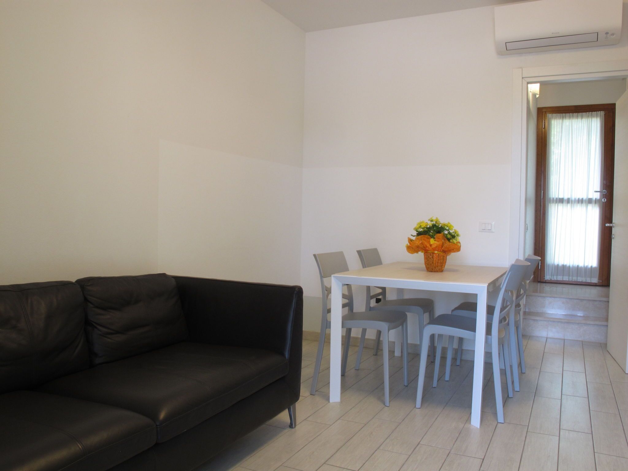 A living room with a black leather sofa, a dining table with chairs, and a potted plant.