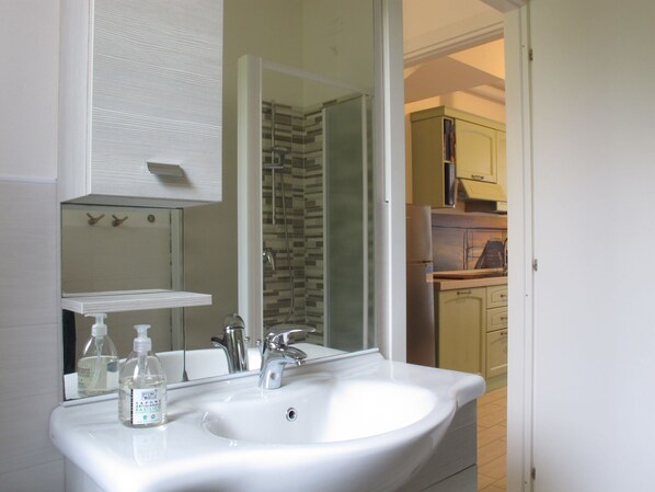 A bathroom with a white sink, a mirror, and a shower. - Veronica by Interhome (Lido di Volano)